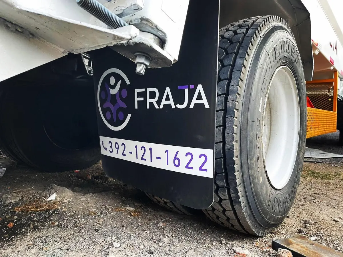 Lodera negra con logotipo y teléfono instalada detrás de la llanta de un camión de carga